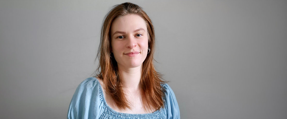 Louise Harmsund. En ung person i ljusblå blus står framför en vägg och ler.