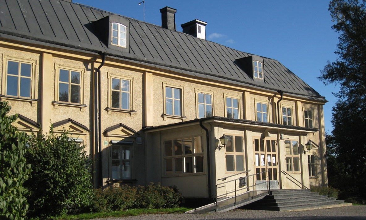 En gul herrgårdsbyggnad i solsken och blå himmel i bakgrunden.