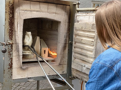 Bild: Deltagare i Happis Arts & Crafts anv&auml;nder t&auml;nger f&ouml;r att placera en lerskulptur i en ugn.